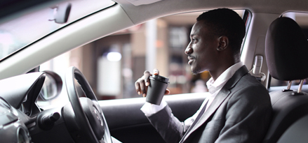 Car driver smiling and drinking coffee while parked at a Mobil station.