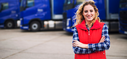 Woman truck driver smiling standing in front of a fleet of trucks.