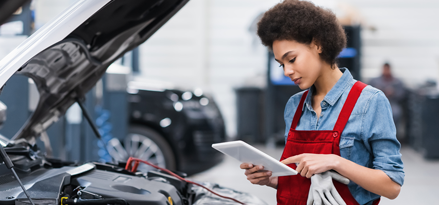 A female mechanic wearing a red apron running diagnostics on a car s engine. With a focused precision, she carefully analyzes the readings from her tablet.