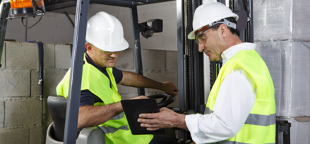 Two construction workers look at tablet in warehouse