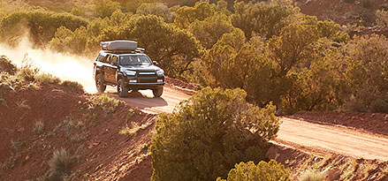 A sport utility vehicle driving down a dirt road in the mountains.