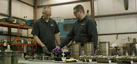 two technicians working on truck parts laid out on a table