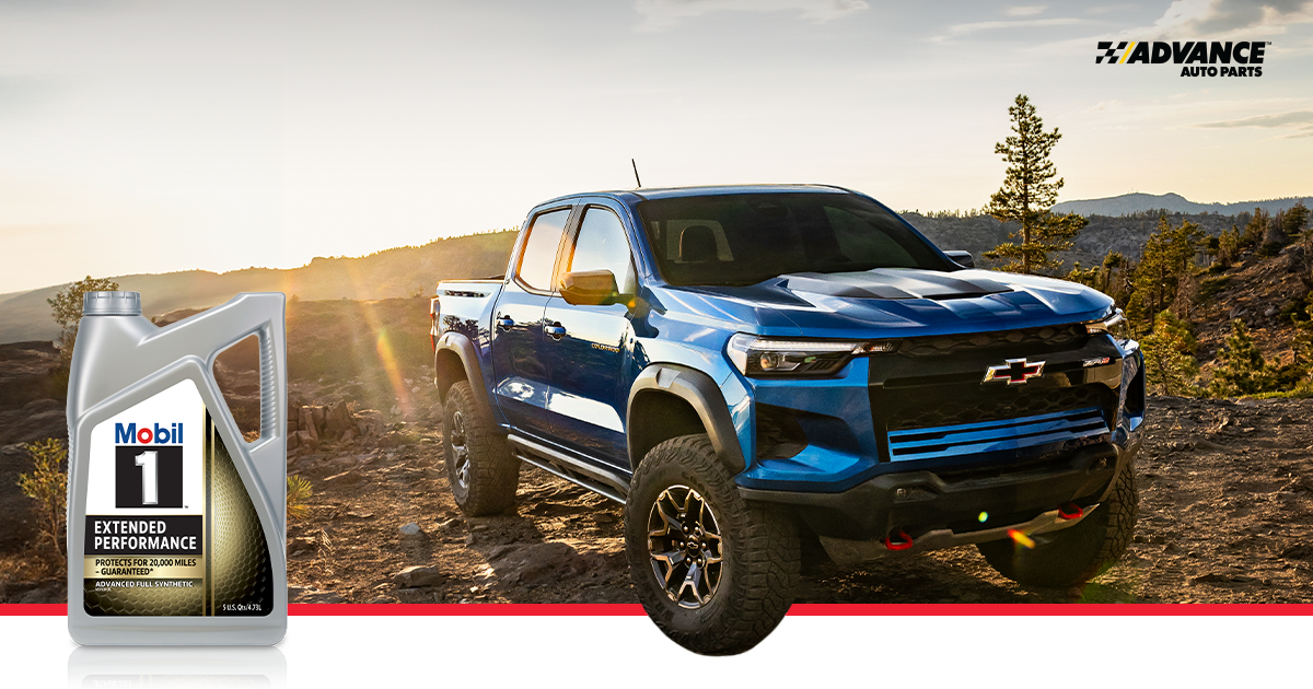 Blue Chevrolet truck drives over rocky terrain with a sun flare in the background. Mobil 1 motor oil bottle in the foreground. 