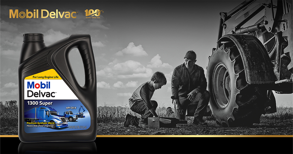 A black and white photo of a farmer and his son who are both kneeling down beside a tractor. A bottle of Mobil Delvac 1300 Super sits in the foreground.