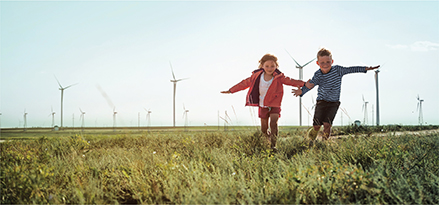 Children playing in grass field with wind turbines in background